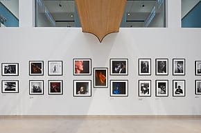 Art gallery wall showcasing a collection of framed black and white photographs with spotlights and high ceiling.