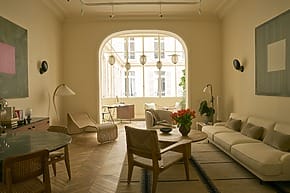Modern living room with beige furniture, wooden flooring, and large window letting in natural light.