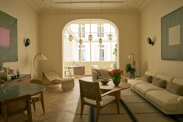 Modern living room with beige furniture, wooden flooring, and large window letting in natural light.