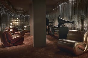 Stylish retro lounge with plush chairs, gramophone, and metallic walls creating a vintage atmosphere.