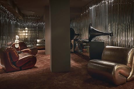 Stylish retro lounge with plush chairs, gramophone, and metallic walls creating a vintage atmosphere.