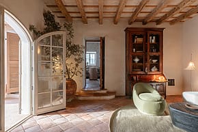 Cozy living room with rustic decor, arched doorway, wooden ceiling beams, and a vintage cabinet.