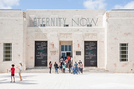Front view of museum entrance with "Eternity Now" sign and people entering on a sunny day.