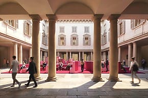 People walking through a sunlit courtyard with columns and a modern seating area in the center