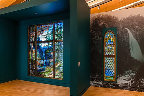 Stained glass windows displayed in an art gallery, showcasing scenic landscapes and decorative patterns.