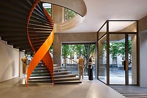 Spiral staircase with orange accents in a modern, stylish interior near glass doors and mannequins.