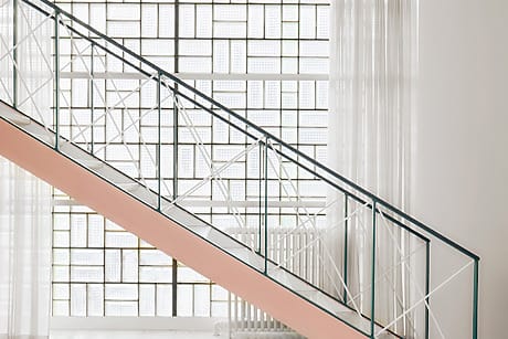 Modern staircase with geometric metal railing and large grid-patterned window in a bright, minimalist interior space.