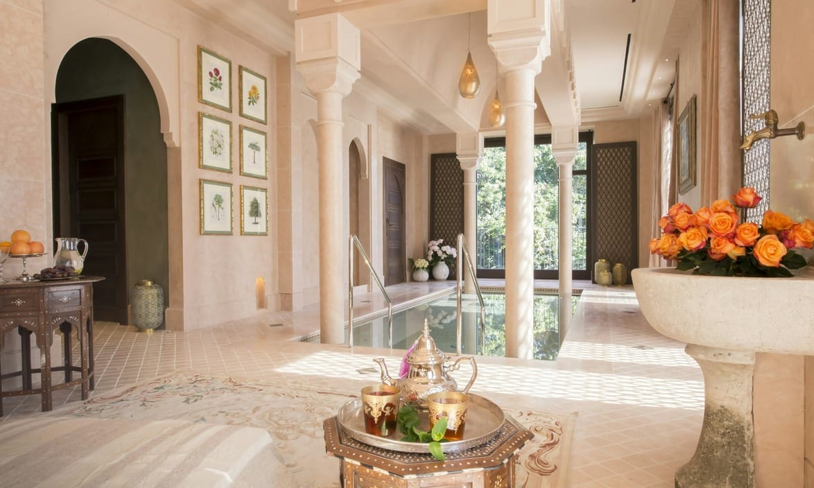 Hammam Suite at Palazzo Parigi Milan, a luxurious indoor spa room with ornate columns, a central pool, and a decorative tray with tea set in the foreground.