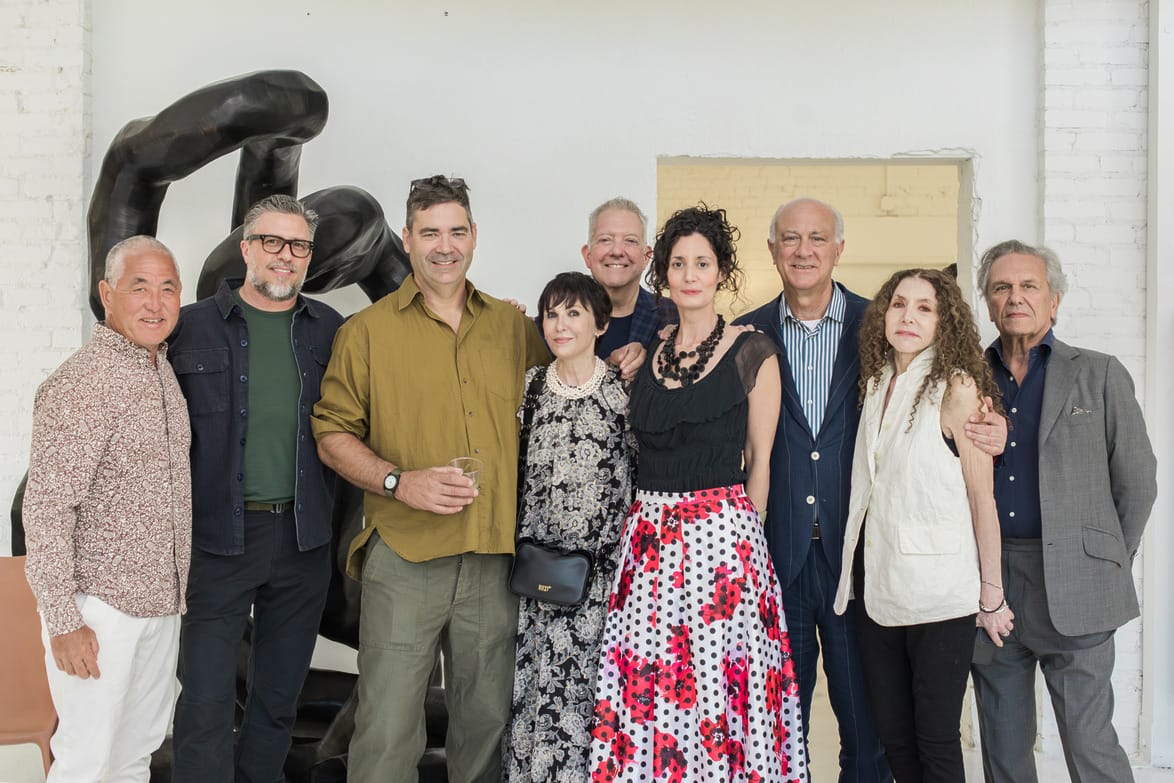 Group of people standing together indoors, smiling at the camera, with an abstract statue in the background.