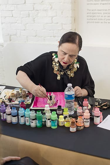 Artist painting on fabric at a table with colorful paints and tools.