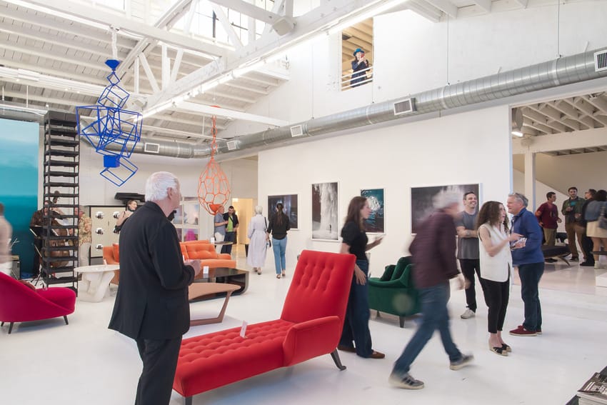 Guests mingle at a modern art gallery event, featuring colorful furniture and contemporary sculptures.