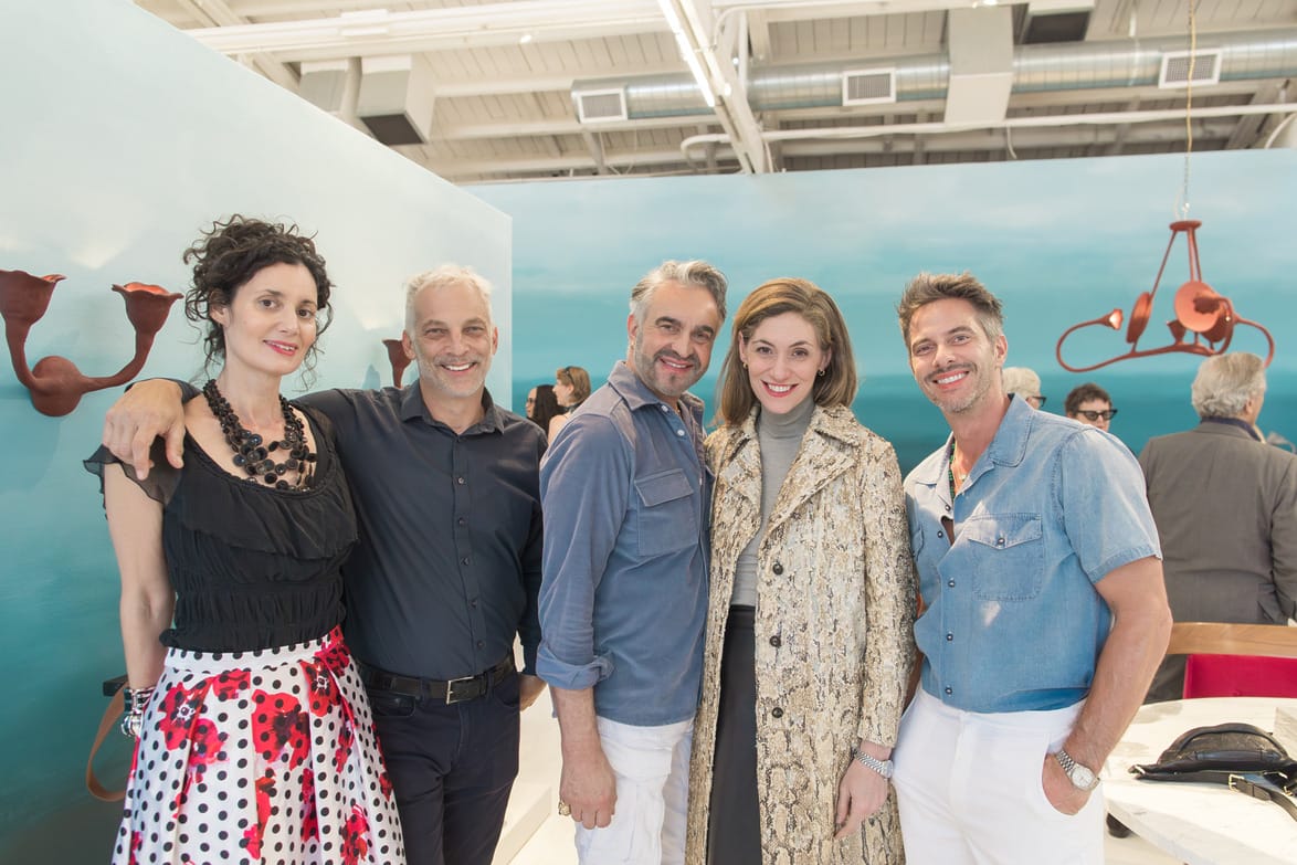 Group of five people posing together in an art gallery setting with artwork in the background.