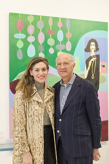 Two people standing in front of a colorful painting with abstract shapes and a figure in the background.
