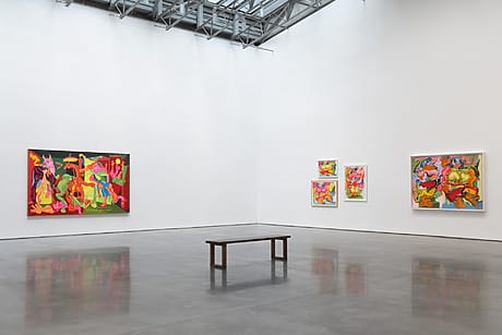 Modern art gallery with colorful abstract paintings displayed on white walls and a wooden bench in the center.