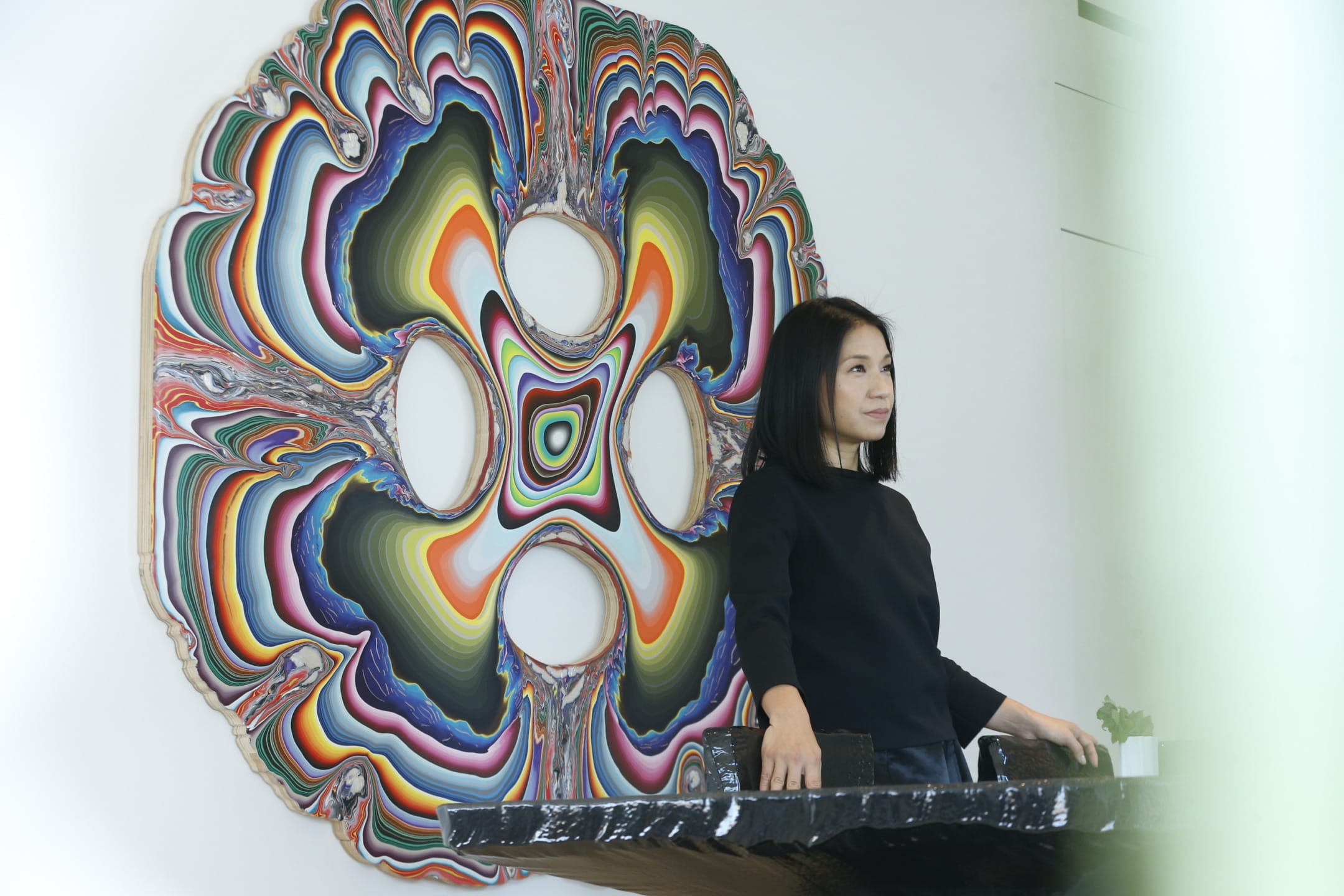 Woman standing at a table with colorful abstract artwork on the wall behind her.