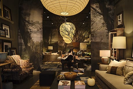 Cozy living room with warm lighting, large paper lanterns, sofas, armchairs, and a coffee table with decorative items.