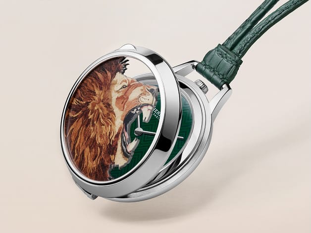 Luxury wristwatch with open case revealing a lion illustration on the inner cover, set against a beige background.