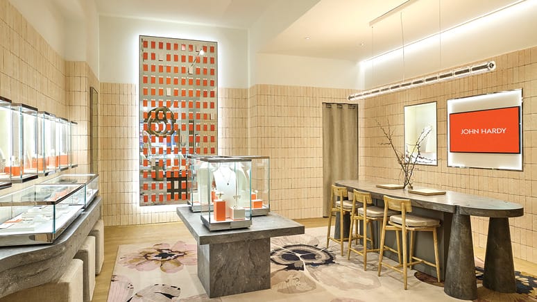 Interior of a modern jewelry store with display cabinets, a table with stools, and warm lighting.