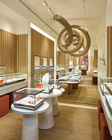 Elegant jewelry store interior with glass display cases, warm lighting, and modern decor featuring wooden accents and artistic ceiling fixture.