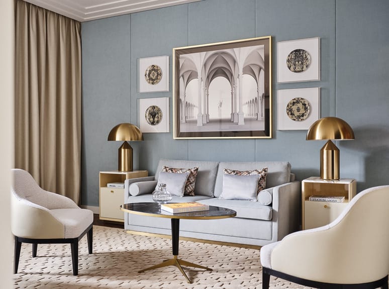 Elegant living room at the Four Seasons Milano with a blue sofa, modern art, gold lamps, and white armchairs around a circular table.