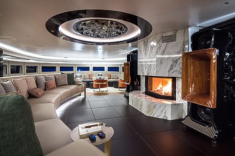 Luxurious yacht interior with modern decor, marble fireplace, circular seating, and ambient lighting.