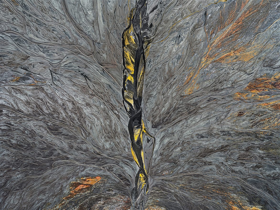 Aerial view of a vibrant abstract landscape with swirling patterns and earthy tones intertwined with streaks of yellow.