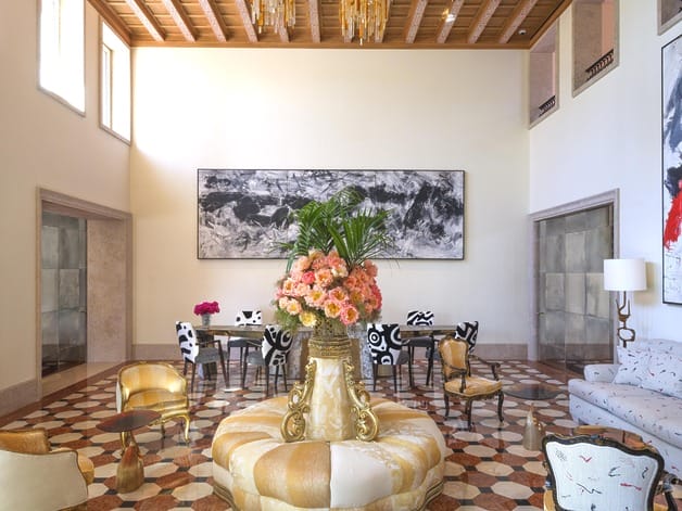 Luxurious hotel lobby with elegant seating, large floral centerpiece, abstract art, and checkerboard flooring.