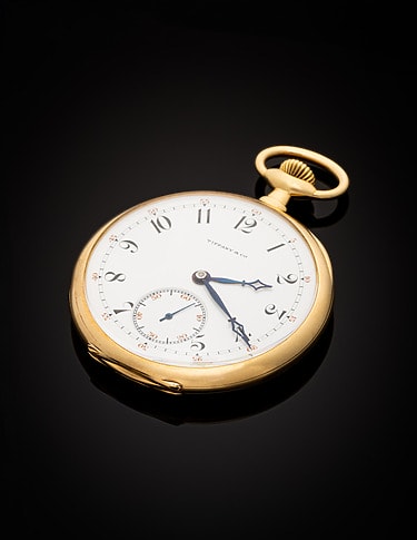 Gold vintage pocket watch belonging to JJ Astor with white face and blue hands on a black background.