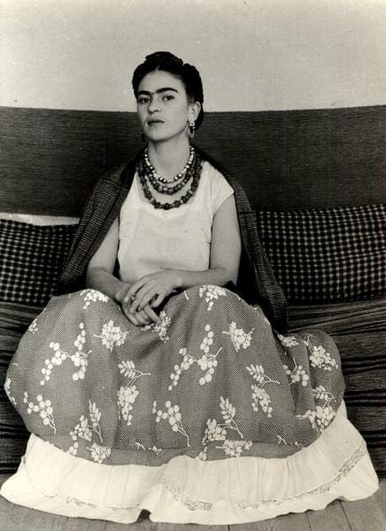Frida Kahlo seated wearing a floral skirt and necklaces, with a shawl draped over shoulders, against a checked cushion, in a photo that was displayed at the Park Avenue Armory for AIPAD.
