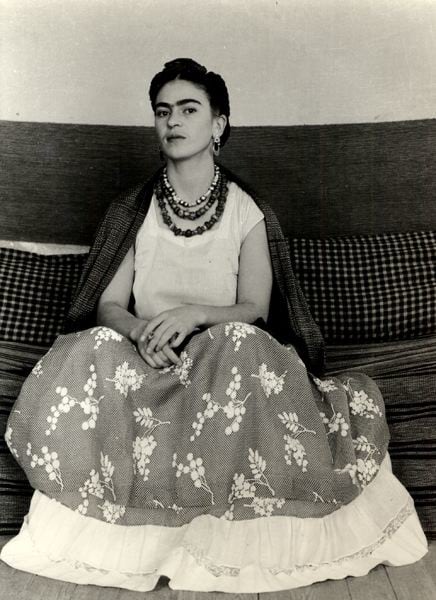 Frida Kahlo seated wearing a floral skirt and necklaces, with a shawl draped over shoulders, against a checked cushion, in a photo that was displayed at the Park Avenue Armory for AIPAD.
