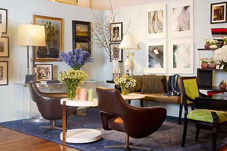 Modern living room with art on walls, brown chairs, floral arrangements on tables, and mixed decor elements.