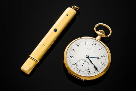 Lot 36 | John Jacob Astor IV's Patek Philippe for Tiffany & Co., 18K Yellow Gold Pocket Watch, Property Of The Astor Family | Estimate: $300,000 - 500,000 Lot 37 | John Jacob Astor IV's Battin & Co. Yellow Gold, Diamond, and Sapphire Pencil Case, Property Of The Astor Family | Estimate: $10,000 - 20,000. Image: Gold vintage pocket watch with white dial and blue accents beside a matching gold cylindrical case on a black surface.