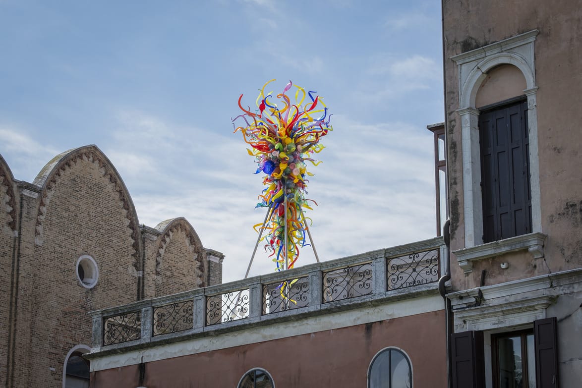 Colorful glass sculpture with swirling shapes atop a building against a clear sky background.