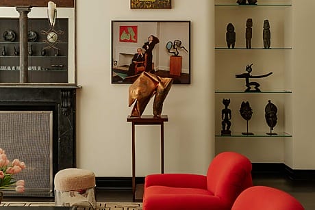 Modern art-filled living room with red chairs, sculptures, and paintings on display.
