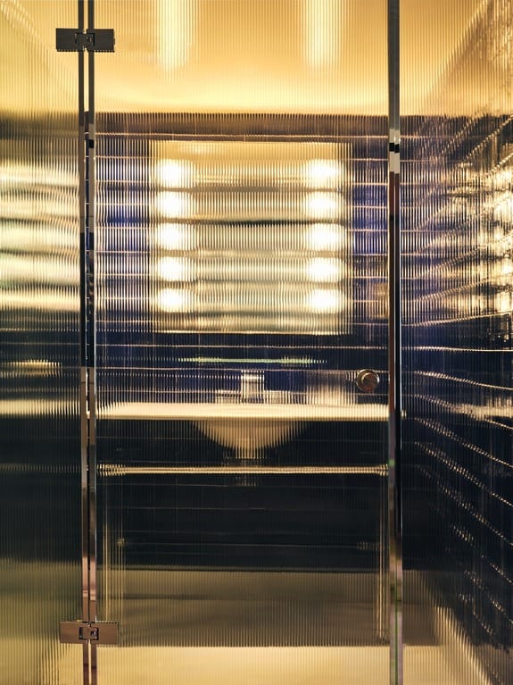 Modern bathroom with textured glass walls, warm lighting, and a sleek sink.