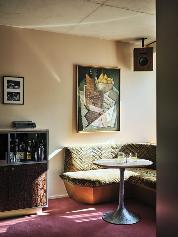 Cozy corner with a modern table, whiskey glasses, and art on the wall, set against a sunlit backdrop in a stylish room.