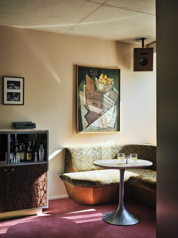 Cozy corner with a modern table, whiskey glasses, and art on the wall, set against a sunlit backdrop in a stylish room.
