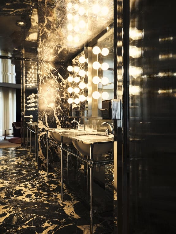 Luxurious bathroom with marble walls and floor, double sinks, large mirrors, and illuminated with spherical lights.