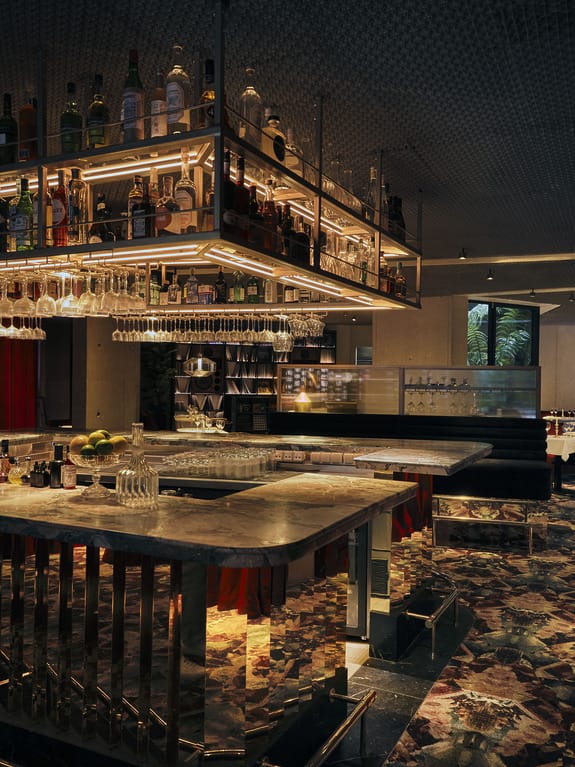 Modern bar interior with an elegant marble countertop, hanging glasses, and various bottles, featuring ambient lighting.