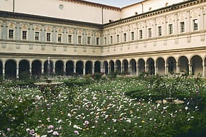 Historic courtyard with arched walkways and a blooming garden filled with colorful flowers in the center.