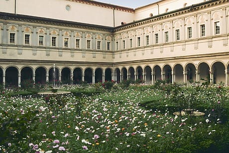 Historic courtyard with arched walkways and a blooming garden filled with colorful flowers in the center.