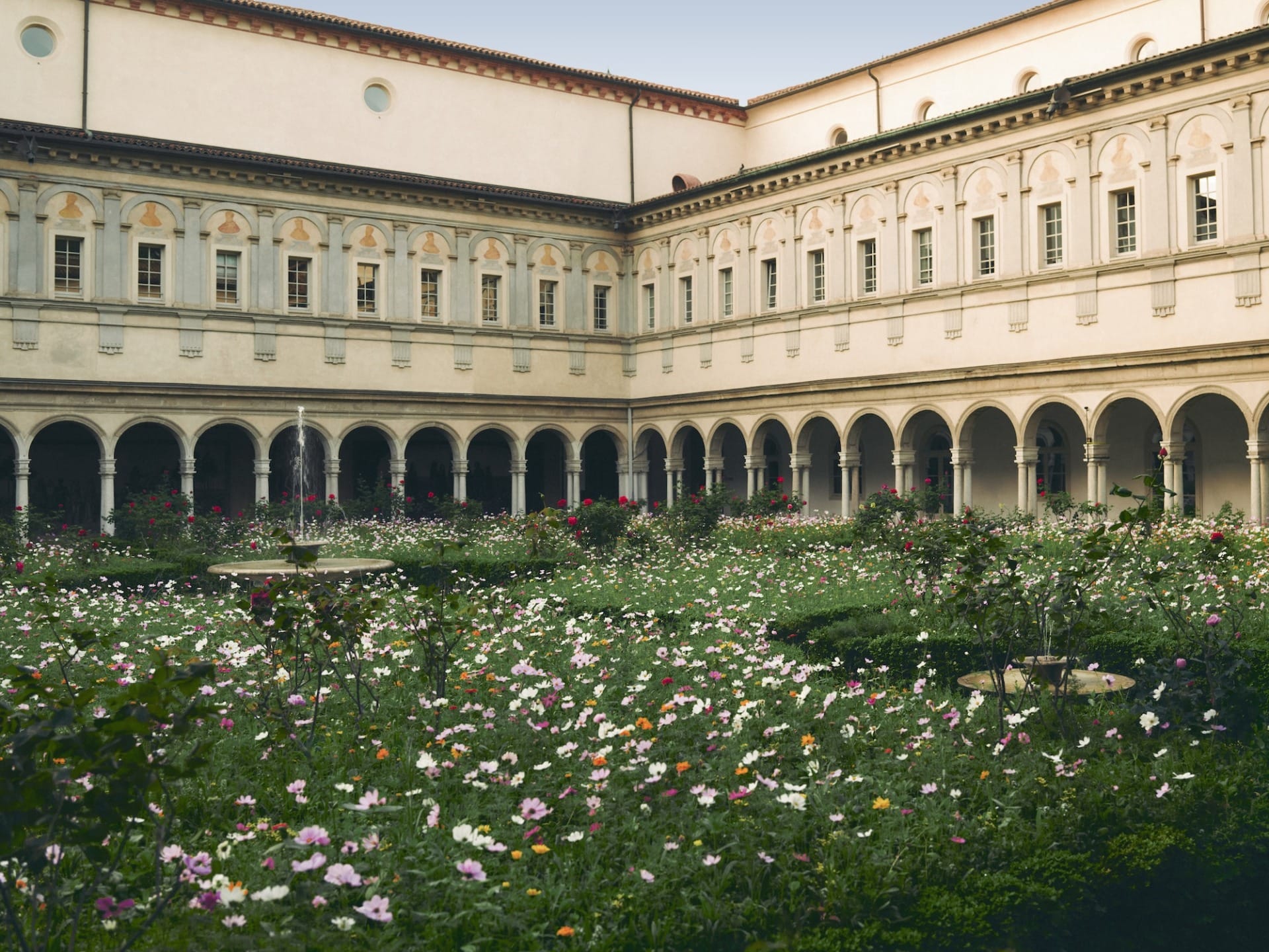 Historic courtyard with arched walkways and a blooming garden filled with colorful flowers in the center.