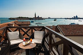 Rooftop patio with two chairs and a table overlooking Venice canals and cityscape with boats on the water.