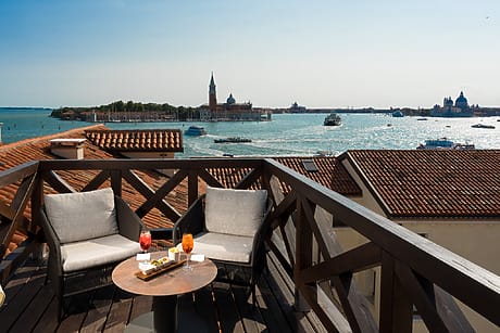 Rooftop patio with two chairs and a table overlooking Venice canals and cityscape with boats on the water.