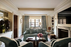 Elegant living room with blue sofas, armchairs, a fireplace, and large window allowing natural light, accented with floral decor.