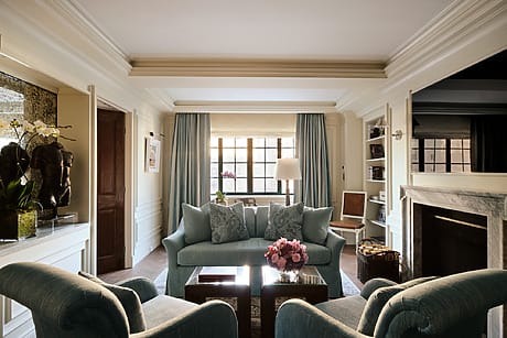 Elegant living room with blue sofas, armchairs, a fireplace, and large window allowing natural light, accented with floral decor.