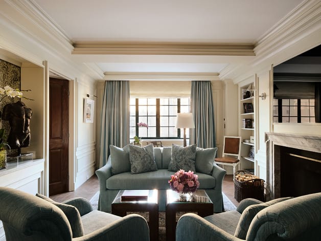 Elegant living room with blue sofas, armchairs, a fireplace, and large window allowing natural light, accented with floral decor.