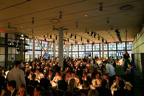 Large banquet hall filled with guests seated at tables, warm lighting, and floral centerpieces creating an elegant atmosphere.