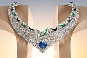 Elegant diamond necklace with emerald accents and a large blue gemstone centerpiece displayed on a decorative background.
