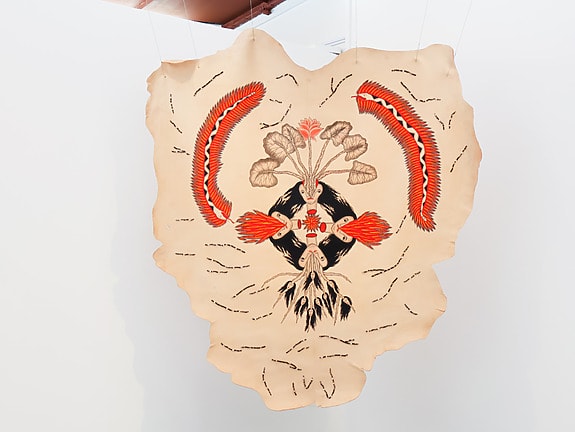 Decoratively painted animal hide displayed on a wall with intricate red and black designs and abstract patterns